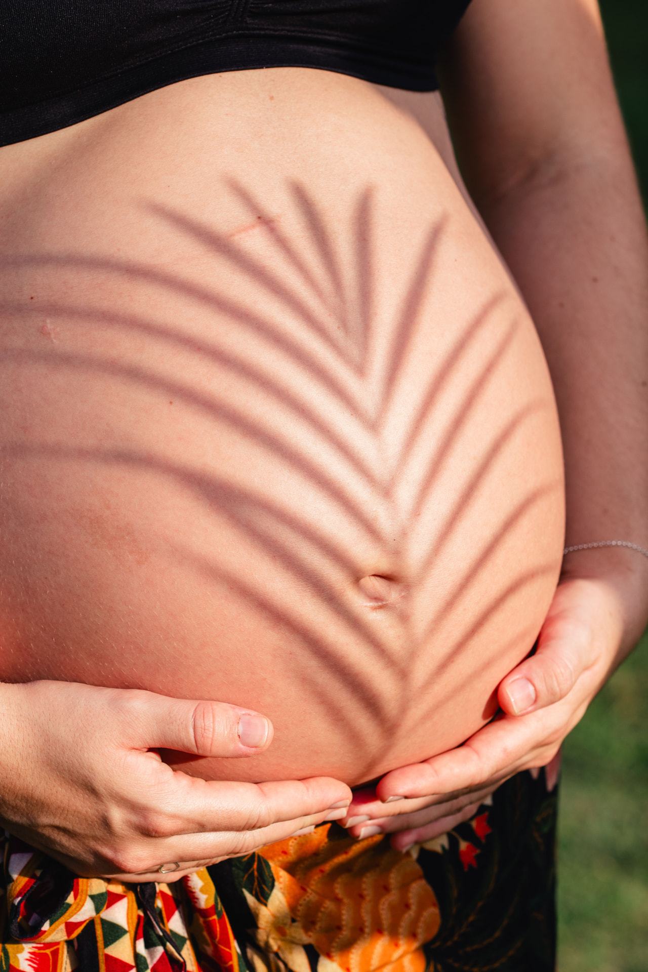 Femme enceinte tenant son ventre, ombre de feuille de palmier