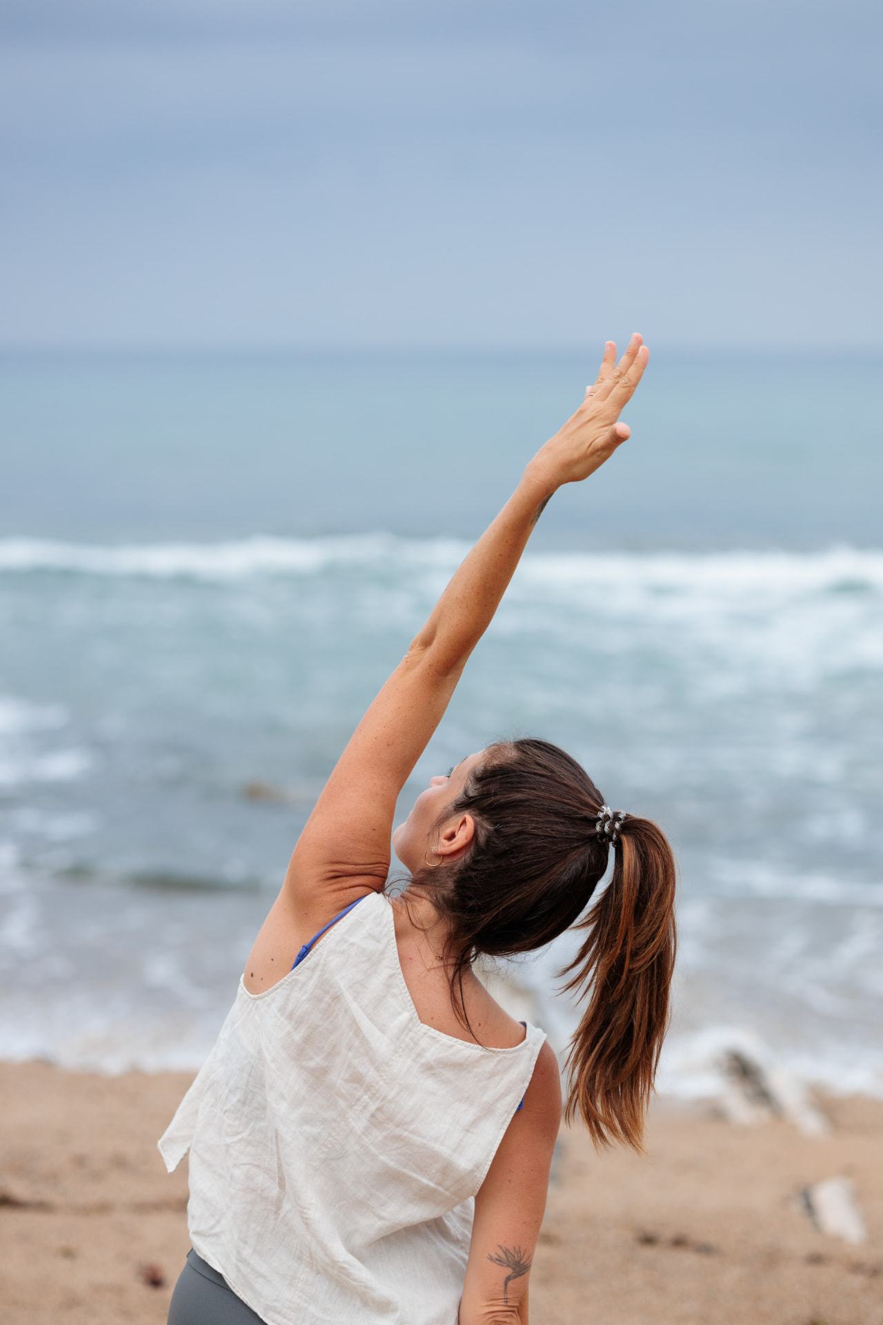 Fanny Gand en posture de yoga sur la plage, un bras levé vers le ciel