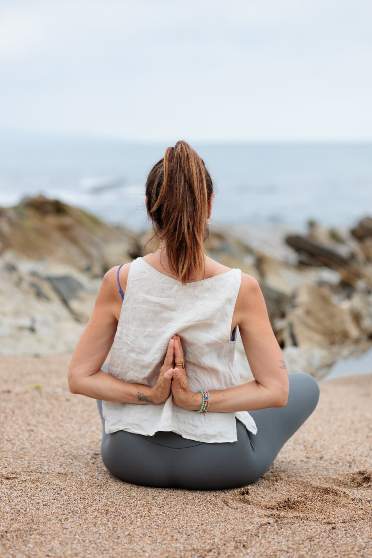 Femme assise en méditation sur la plage, mains jointes dans le dos